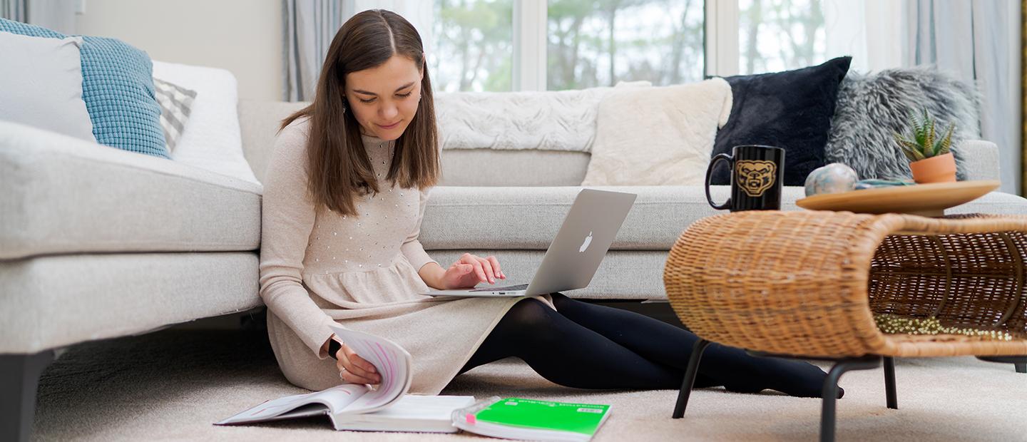 A student working on their computer sitting on the floor