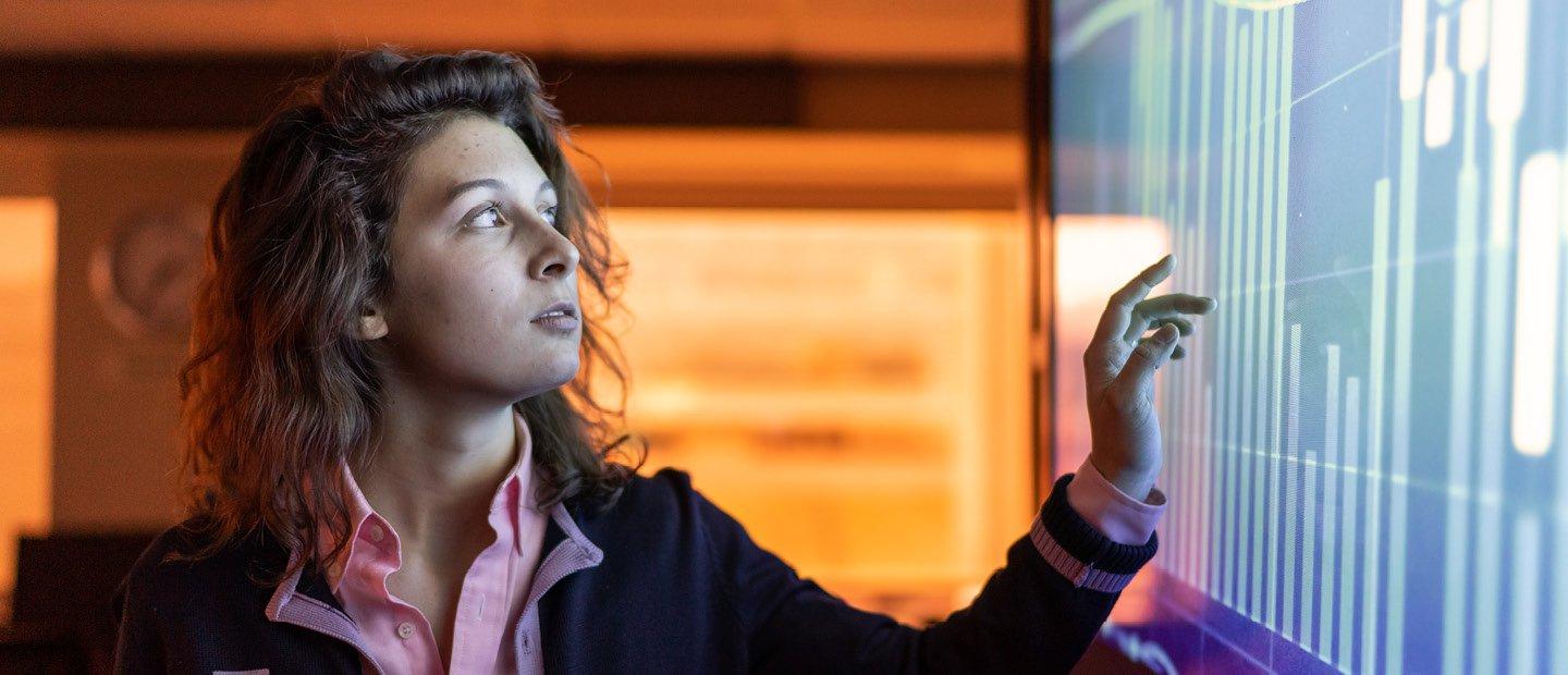 A woman pointing at a large screen with a bar graph on it.